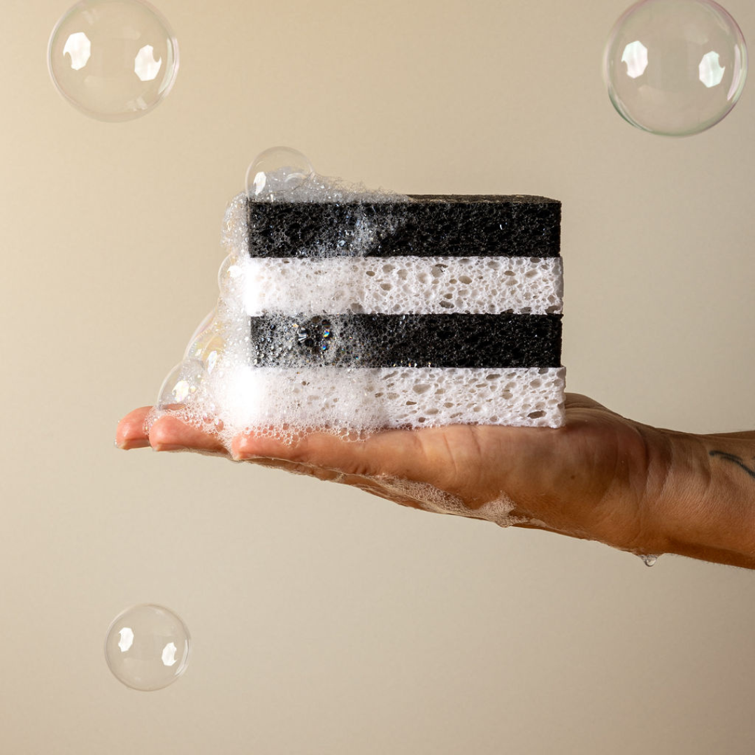 A hand holding a black and white striped sponge with bubbles around it, demonstrating the sponge's ability to expand with water.
